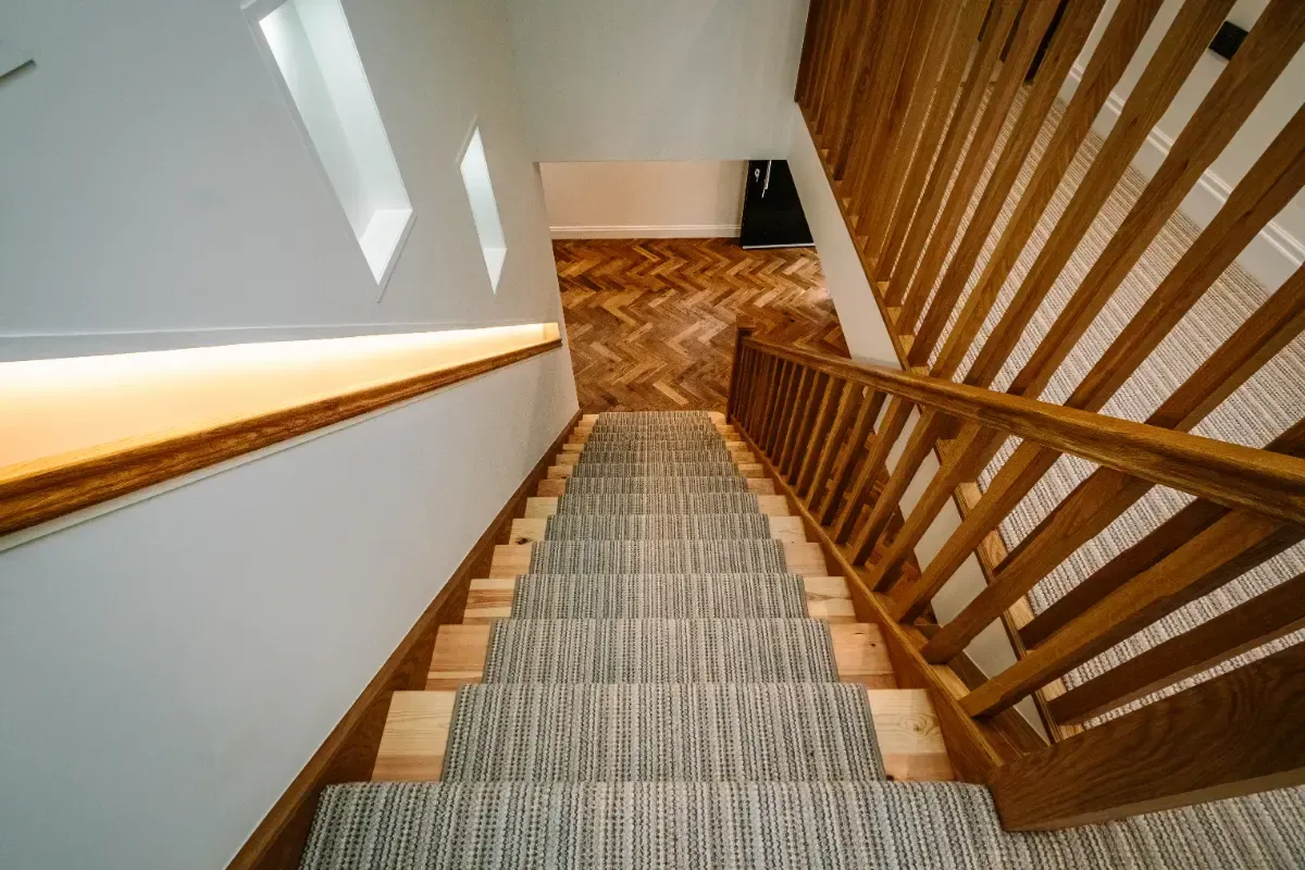 Wooden staircase descending to a lower floor with white walls and a carpet runner