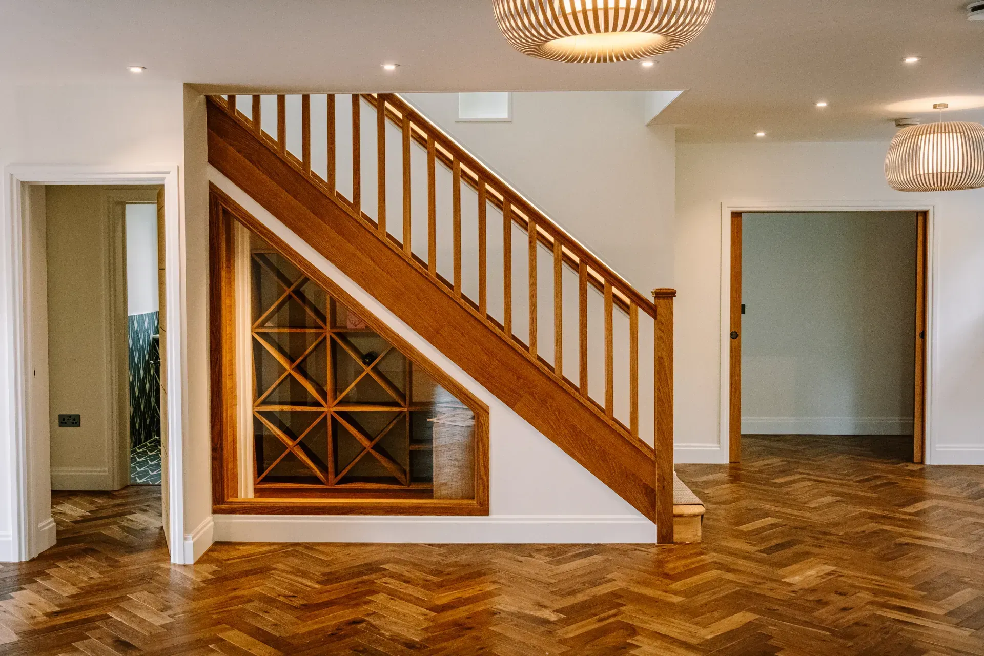 Empty foyer with wood staircase, parquet floor, white walls, and a small decorative wine rack under the stairs.