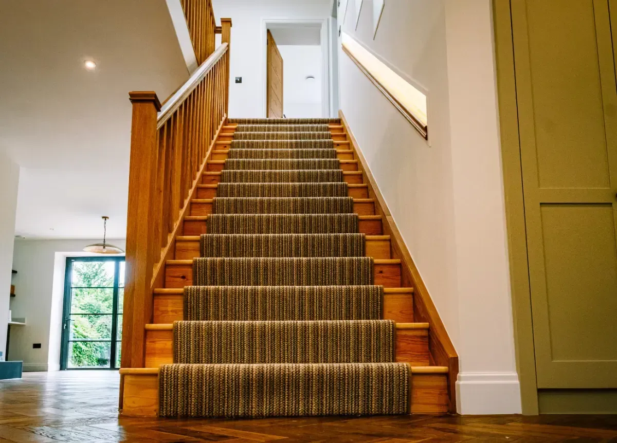 Staircase with patterned carpet, wooden railings, and white walls in a bright home interior