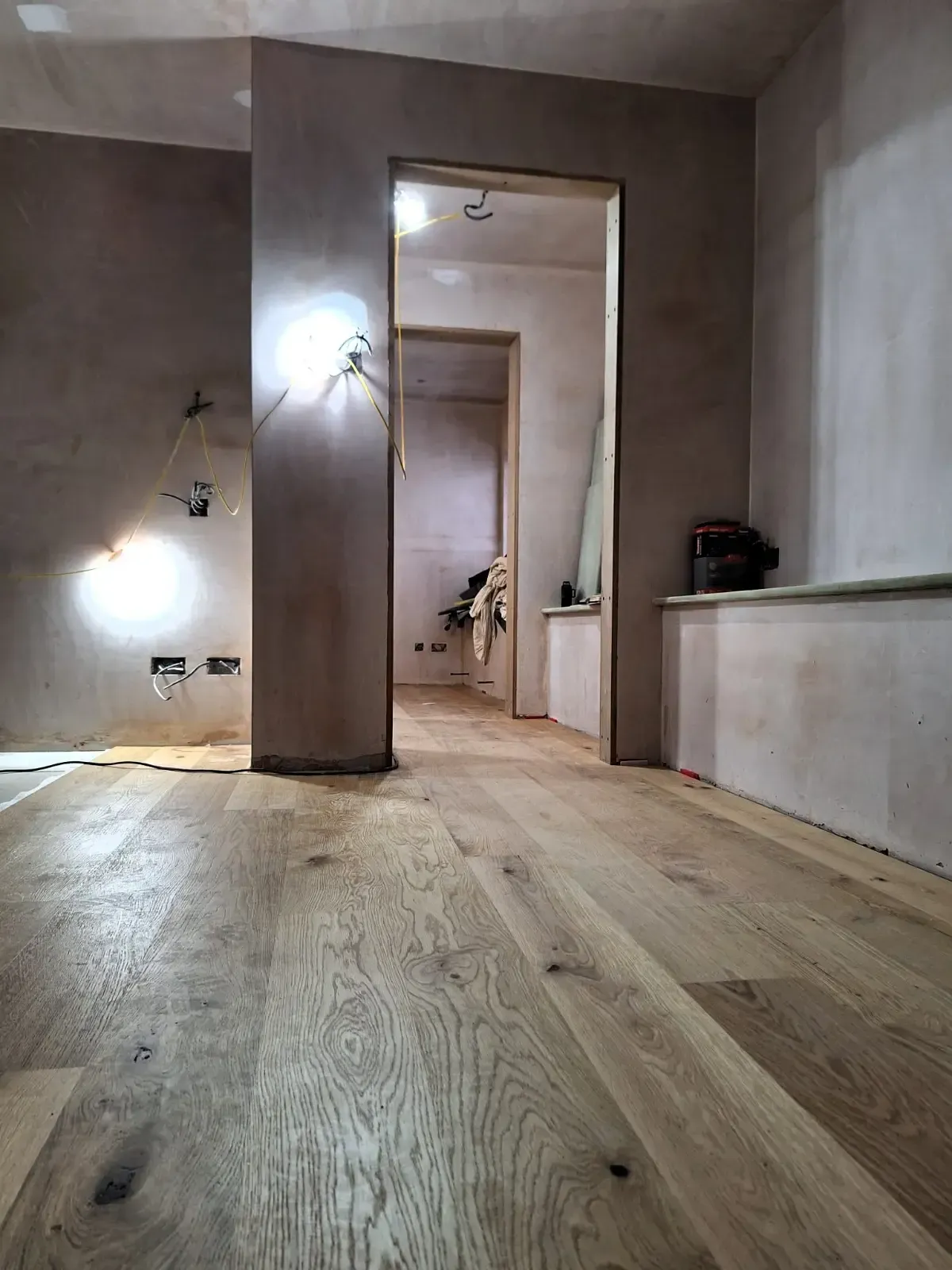 Renovated hallway with light wood floors, brown walls, and a doorway to another room