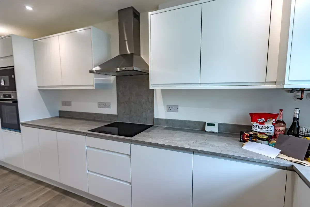 Modern white kitchen with gray countertops, black range hood, and a few items on the right counter