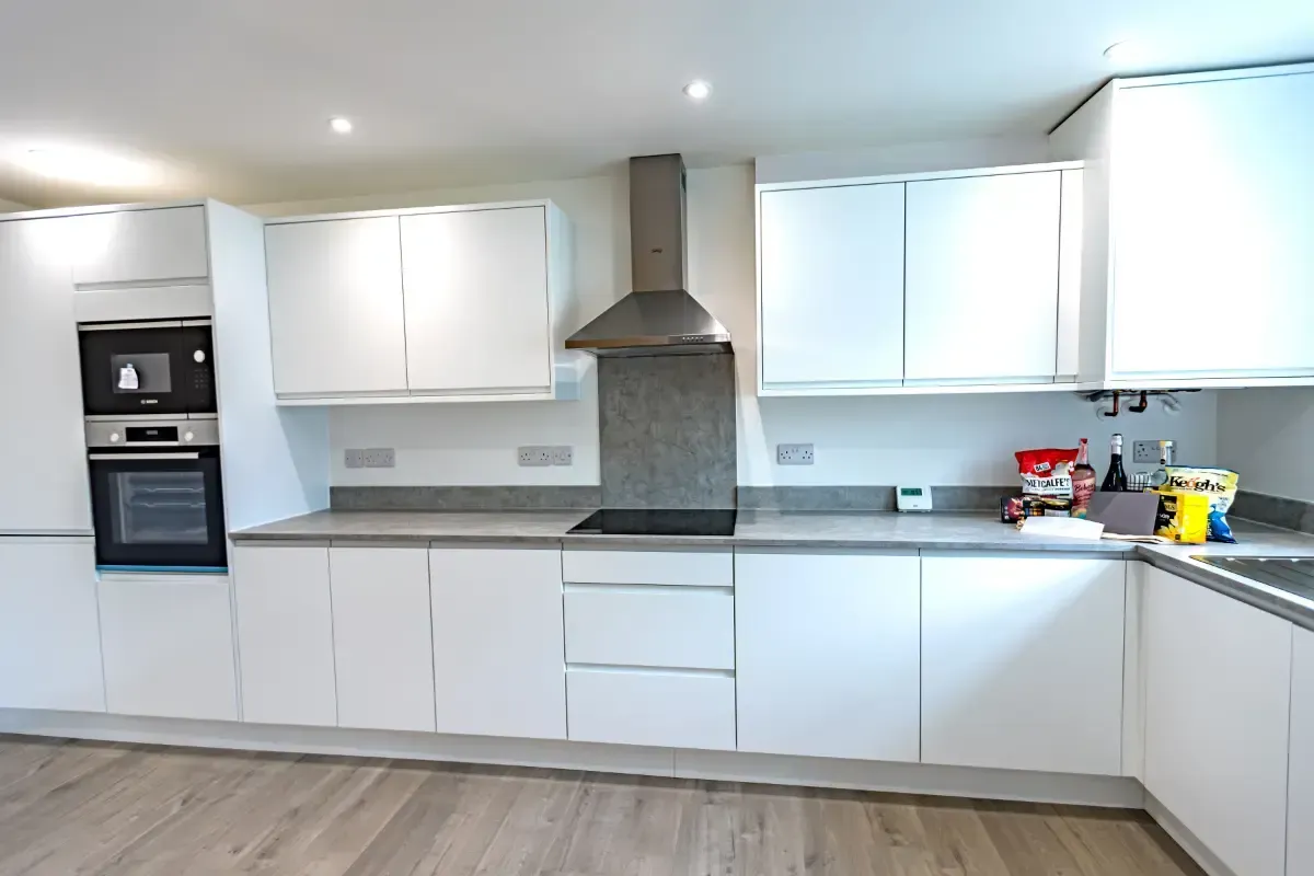 Modern white kitchen with built-in ovens, gray countertops, and wood flooring