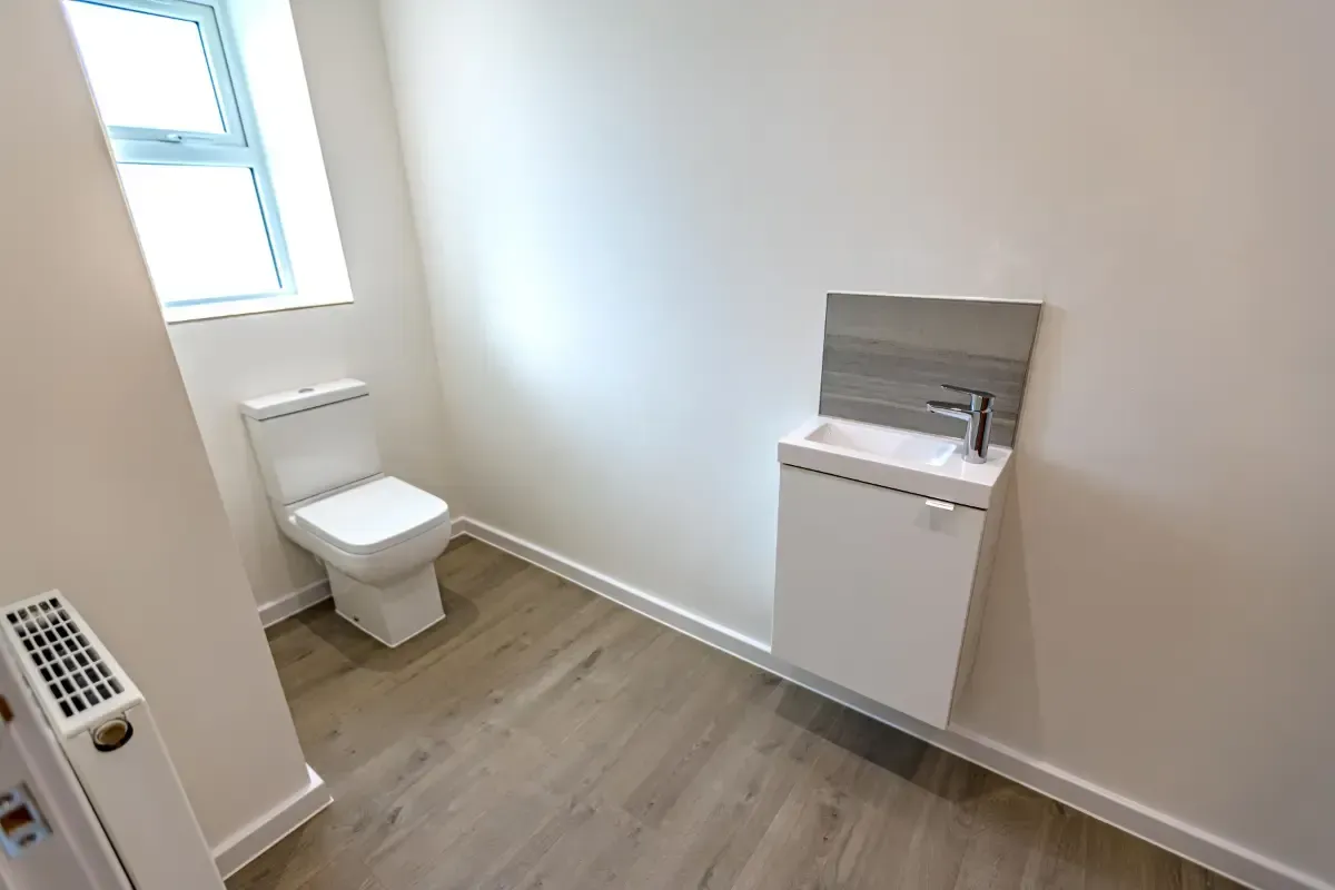Small accessible bathroom with toilet, wall sink, and window on a wood floor.