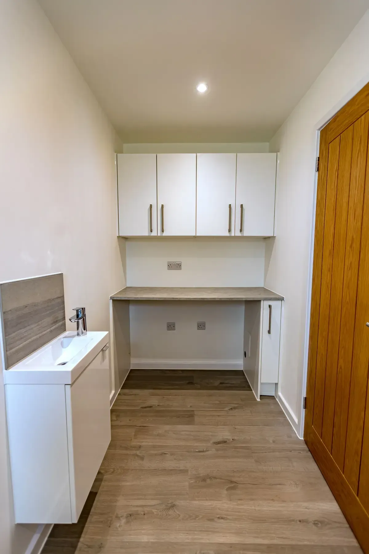 Small white utility room with cabinets, countertop, sink, and wooden door on the right.
