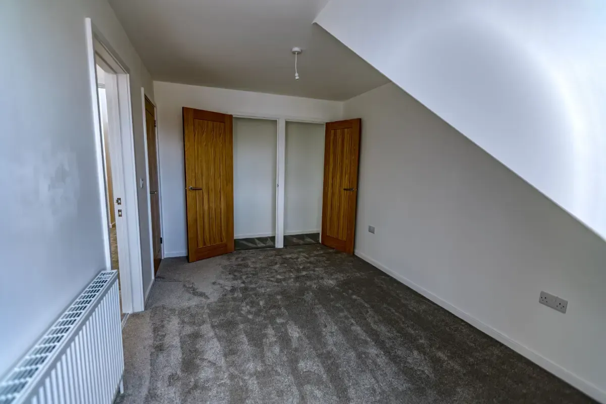 Empty attic room with gray carpet, sloped white ceiling, and two wooden doors.