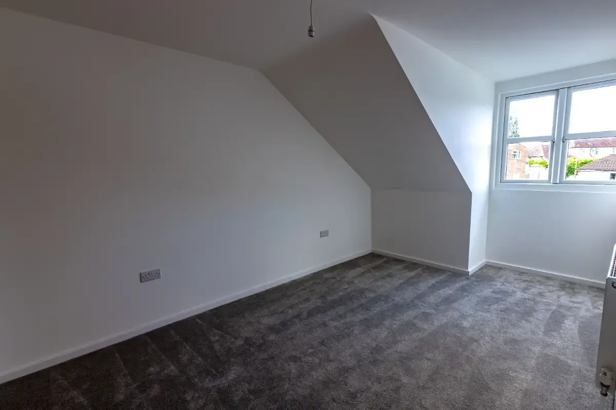 Empty white bedroom with gray carpet and a window at the far end