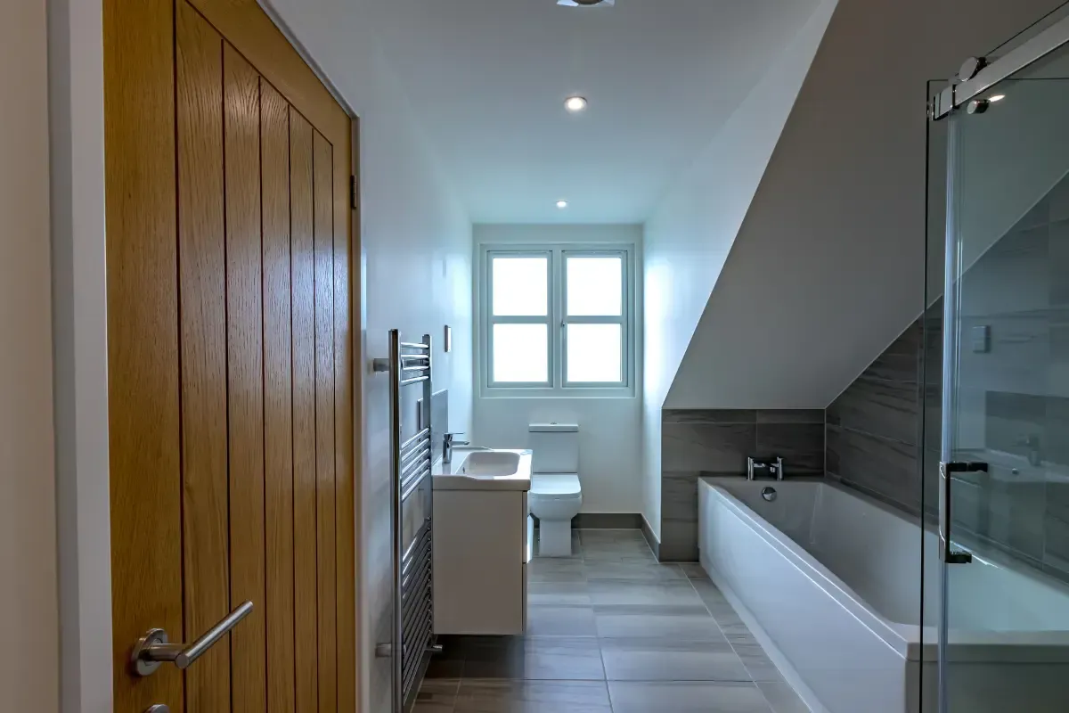 Modern bathroom with bathtub, toilet, sink, shower, and window at the end of a narrow hallway