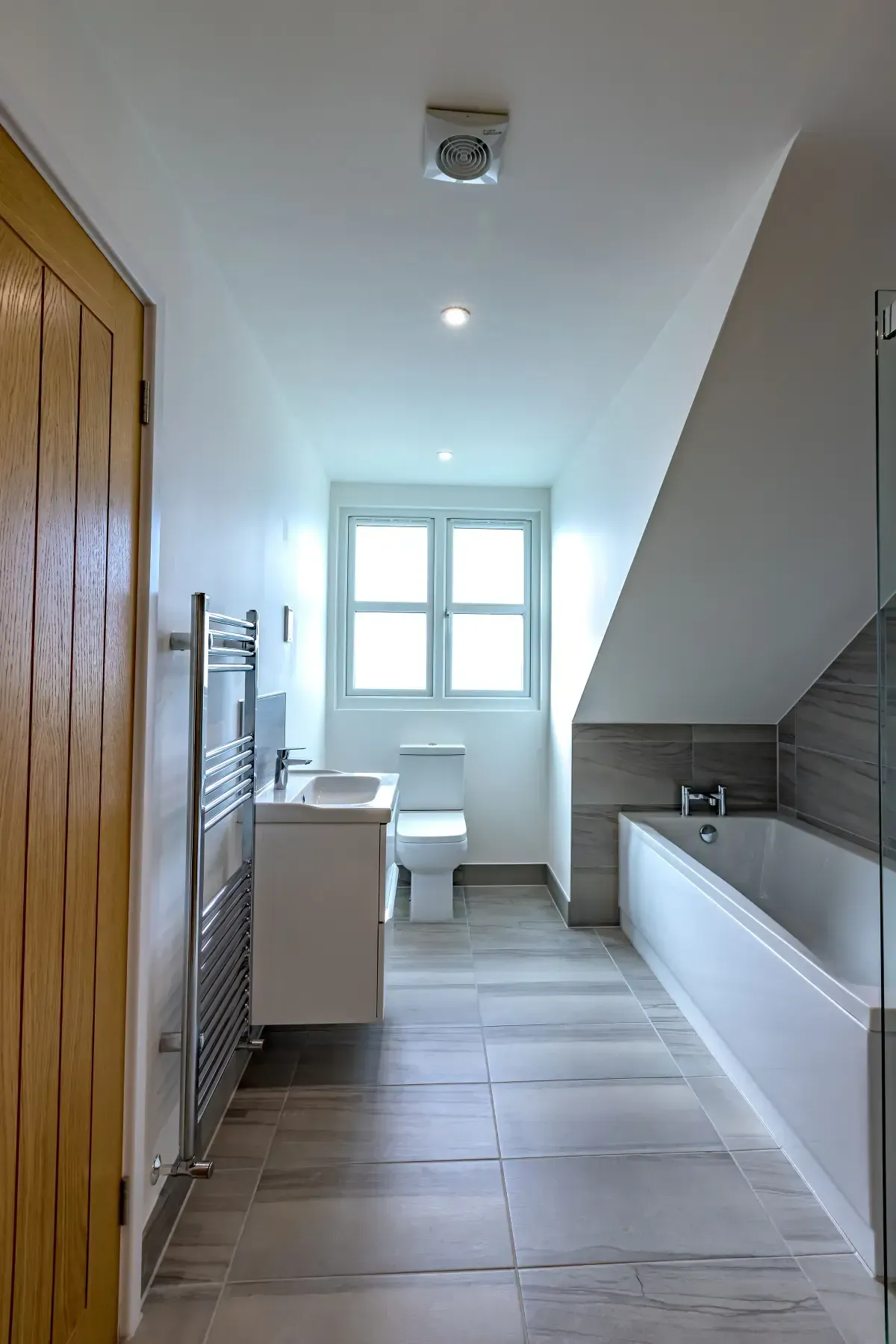 Modern bathroom with bathtub, toilet, sink, window, and tiled floor.