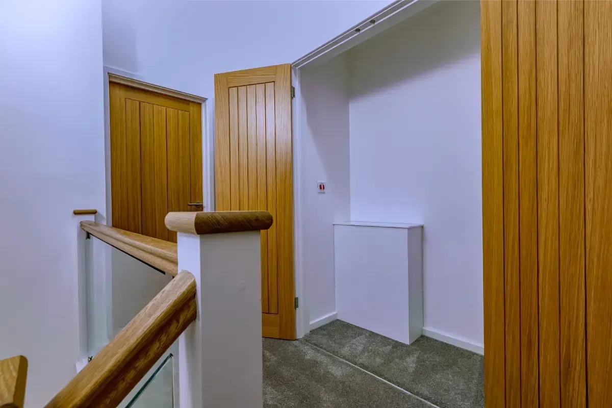 Stair landing with wooden doors, white walls, and a wooden handrail in a hallway