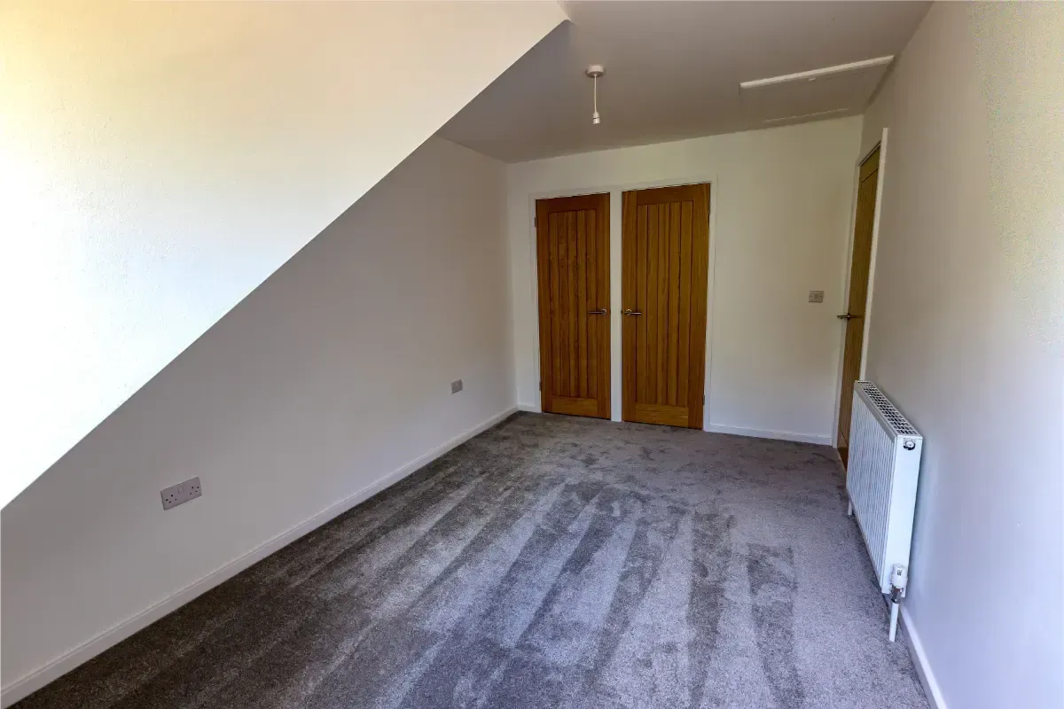 Empty carpeted room with sloped ceiling, wooden double doors, and a radiator on the right wall