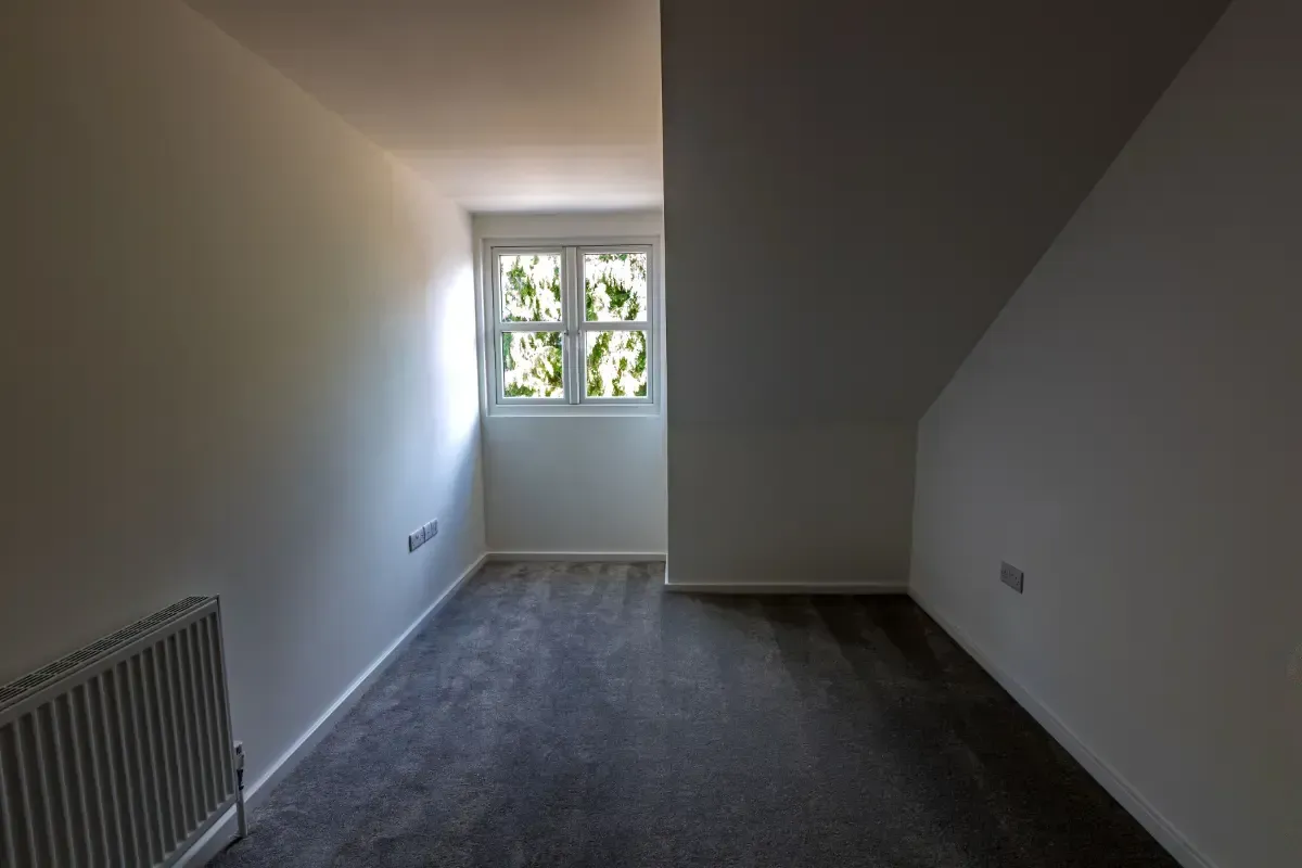 Narrow empty room with gray carpet, white walls, and a small window at the far end