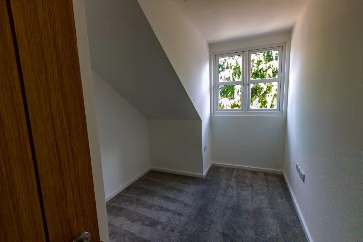 Empty carpeted closet with white walls and a small window at the end.