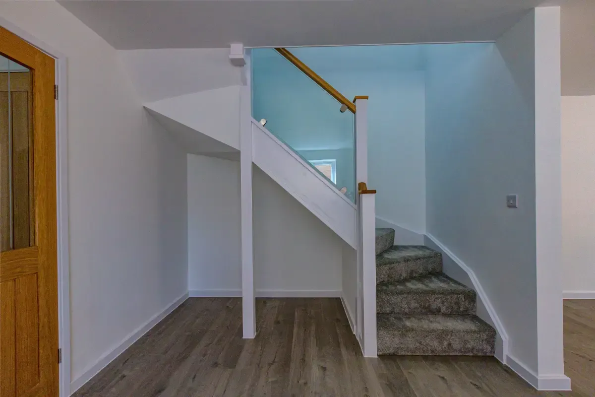 Interior staircase with gray carpeted steps, white walls, and wood flooring beneath the landing