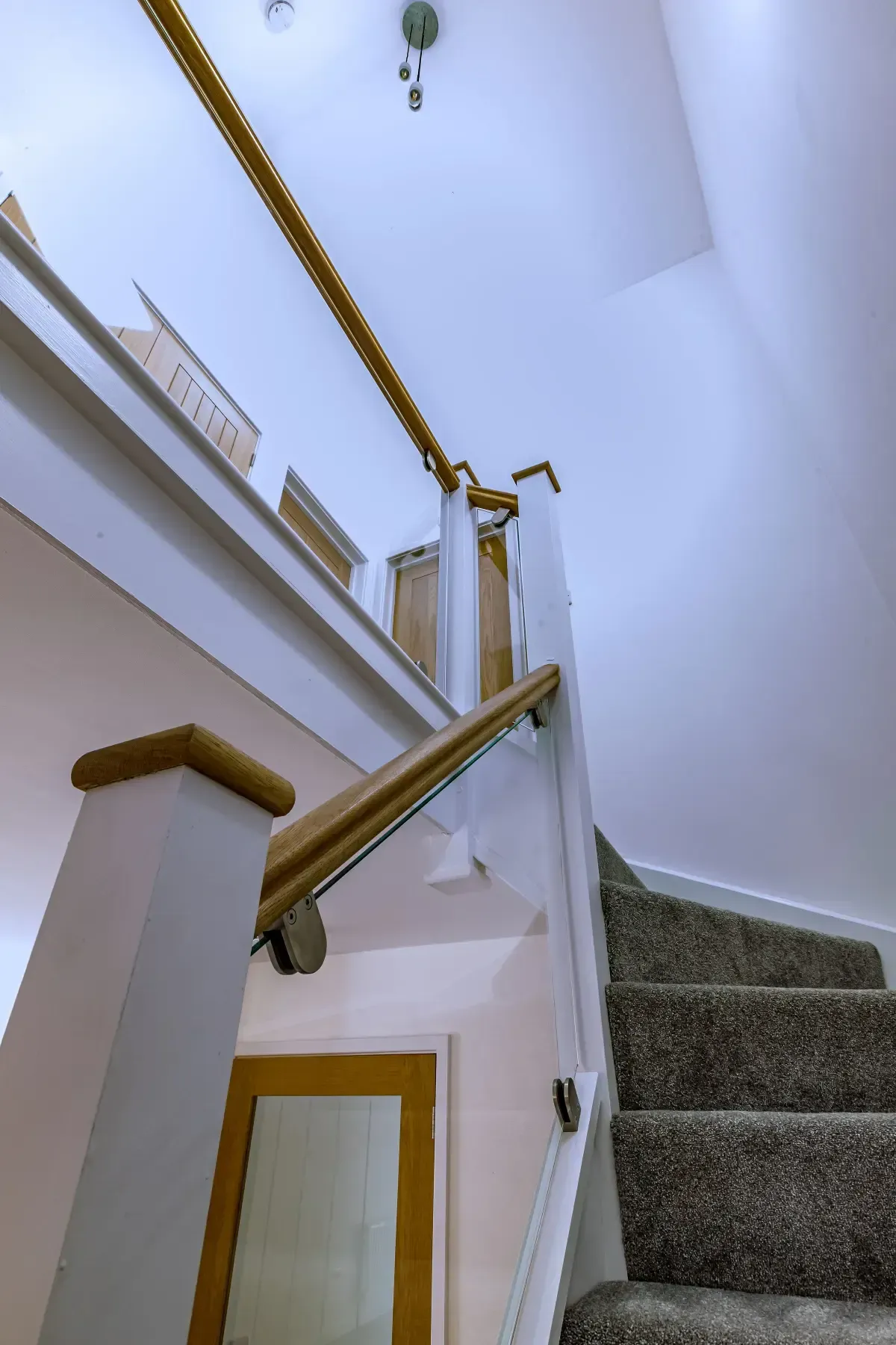 Staircase with carpeted steps, white walls, and gold handrails in a narrow interior hallway.