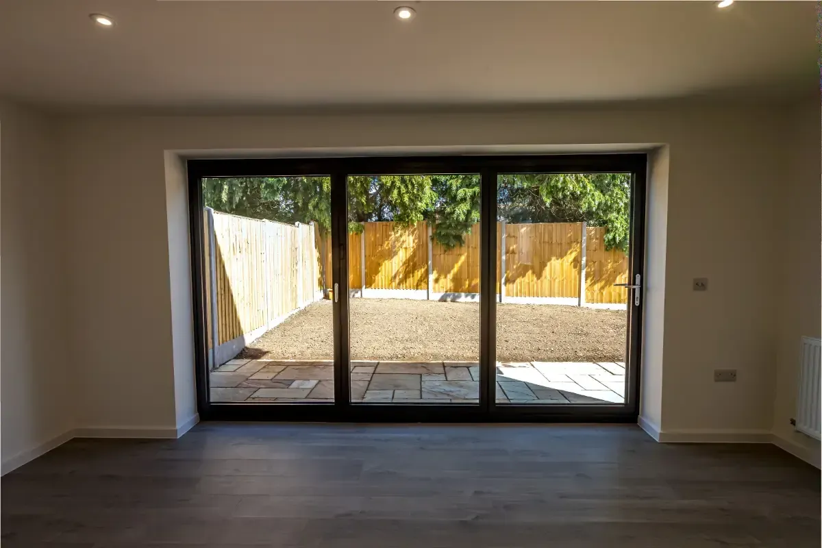 Empty modern living room with large sliding glass doors opening to a fenced patio.