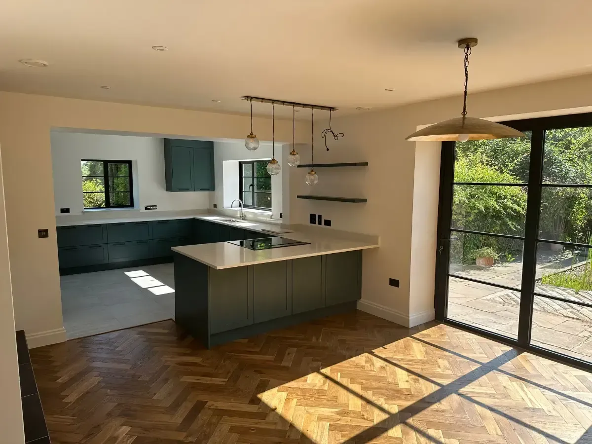 Empty modern kitchen and dining area with teal cabinets, island, wood floor, and sliding glass doors to a patio.