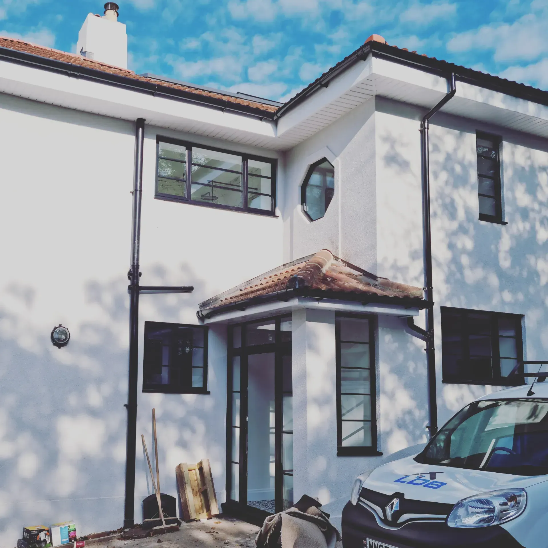 White two-story house with red-tiled roof and parked car in front on a sunny day