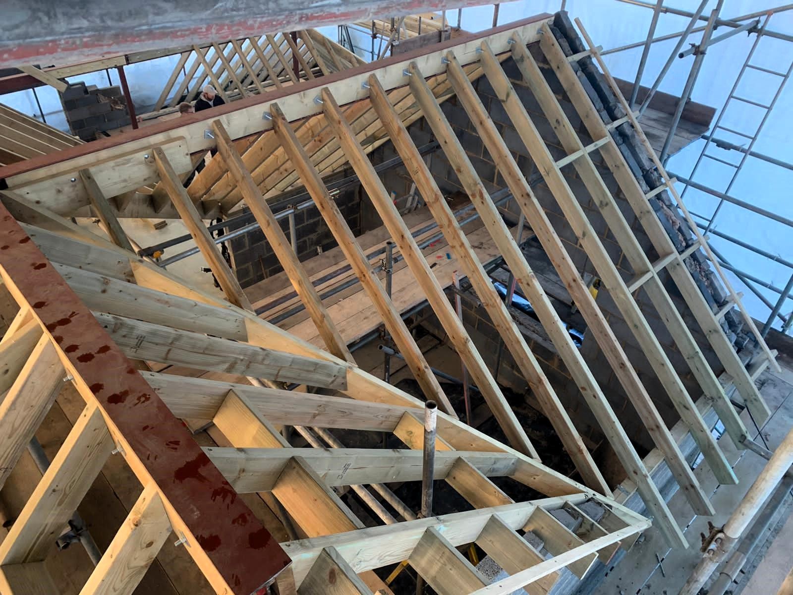 Wooden roof framing under construction with scaffolding and blue sky in the background