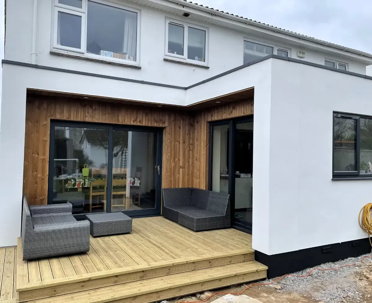 Modern house patio with wooden deck, sliding glass doors, and outdoor seating under a white overhang