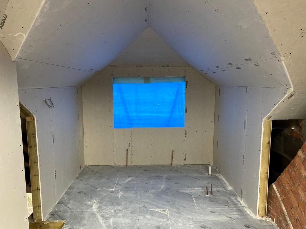 Empty unfinished attic room with white walls, gray floor, and a small blue-lit window.