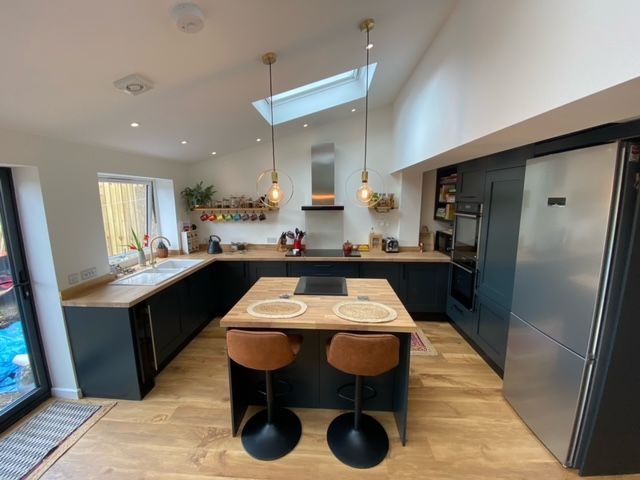 Modern kitchen with black cabinets, wood island, two stools, skylight, and stainless steel appliances