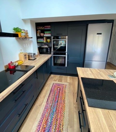 Modern kitchen with dark cabinets, light wood counters, stainless fridge, and colorful runner rug