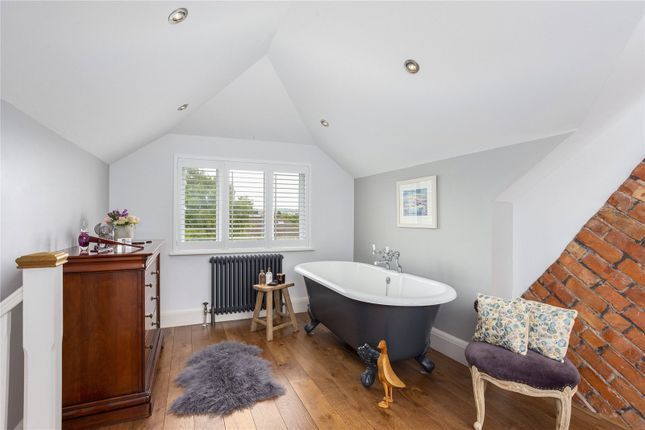 Bright attic bathroom with freestanding tub, window, wood floor, and exposed brick wall