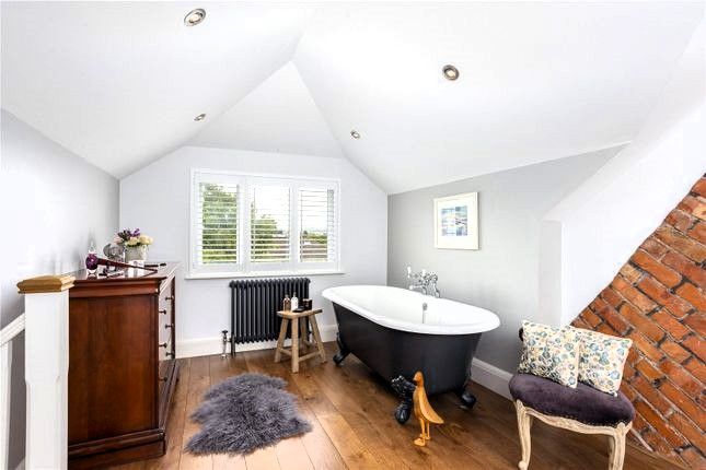 Bright attic bathroom with freestanding tub, white walls, wood floor, radiator, and skylight-like sloped ceiling