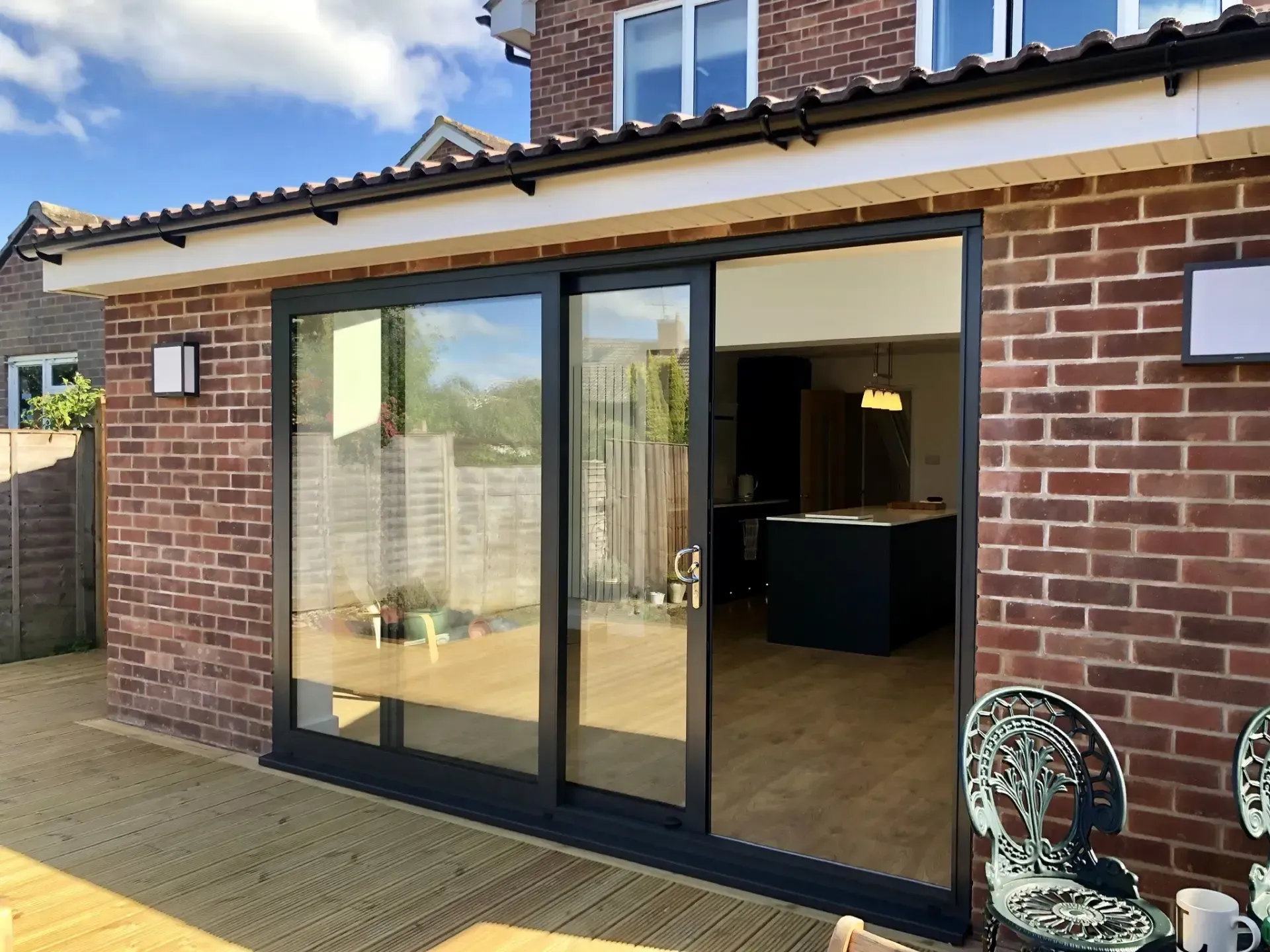 Brick patio with black-framed sliding glass doors opening to a modern kitchen or living room