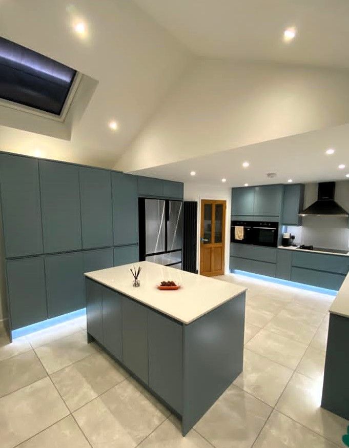 Modern kitchen with blue-gray cabinets, white island, tiled floor, and recessed ceiling lights.