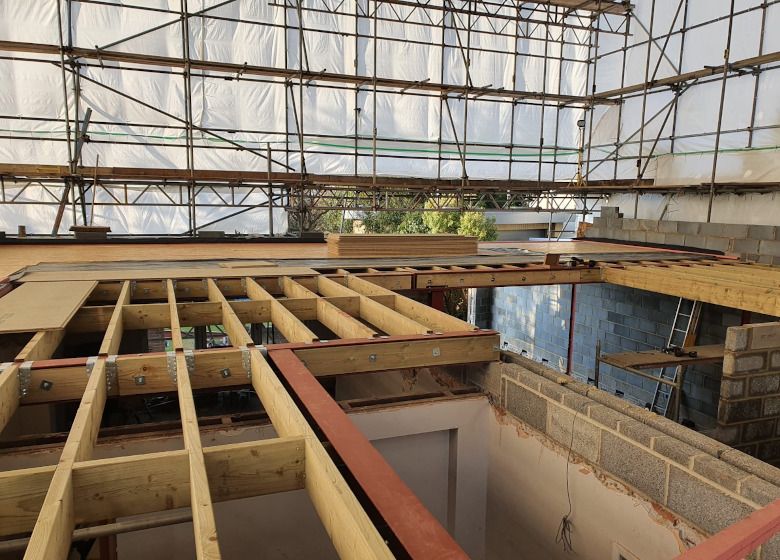 Interior of a building under construction, with exposed wooden framing and scaffolding beneath a high roof.