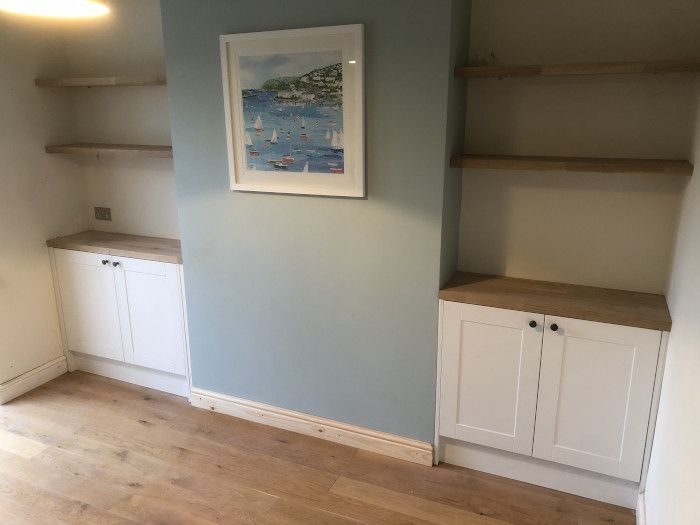 Built-in shelves and cabinets in a light blue room with wood floors and framed wall art.