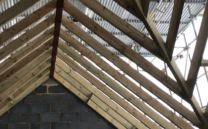 Exposed wooden roof trusses above a cinder block wall under construction
