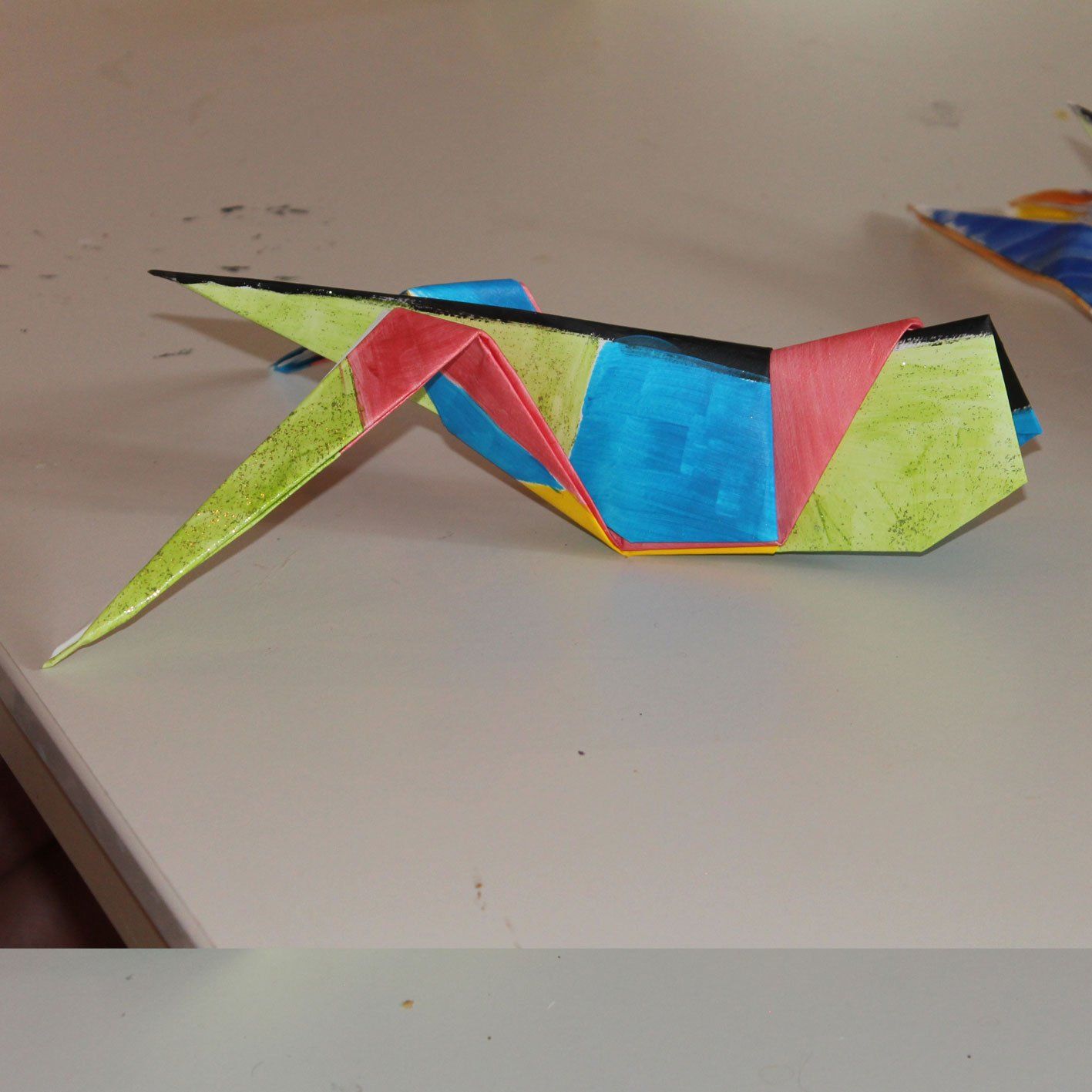 Een kleurrijke origamivogel zit op een tafel
