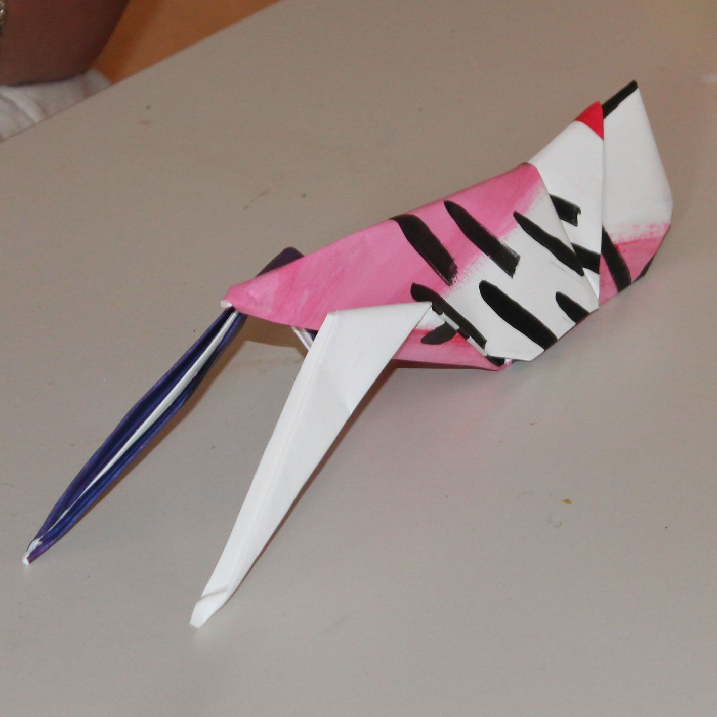 Een roze en witte origamivogel met een blauwe staart