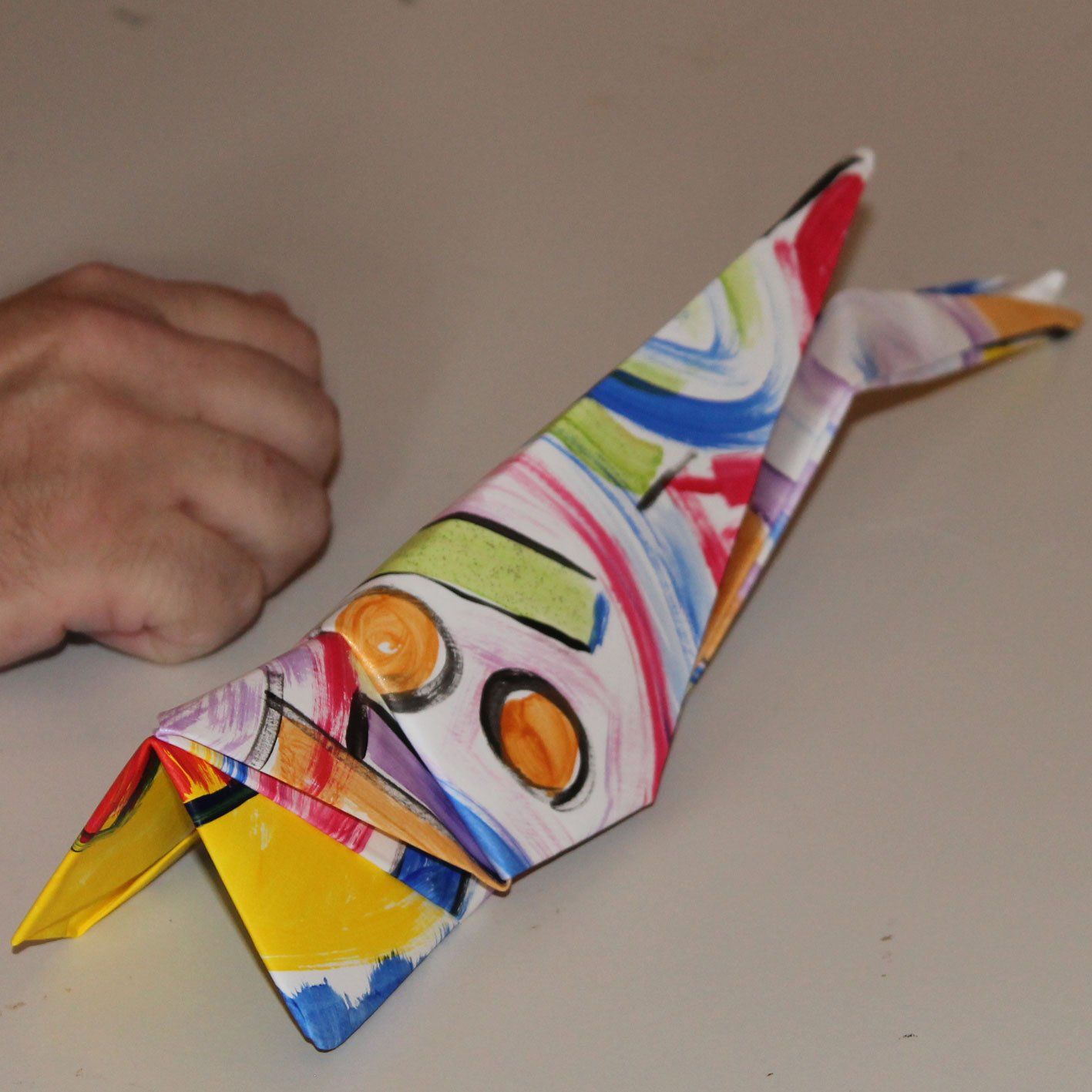 Een persoon houdt een kleurrijke origamivogel met een gele snavel vast