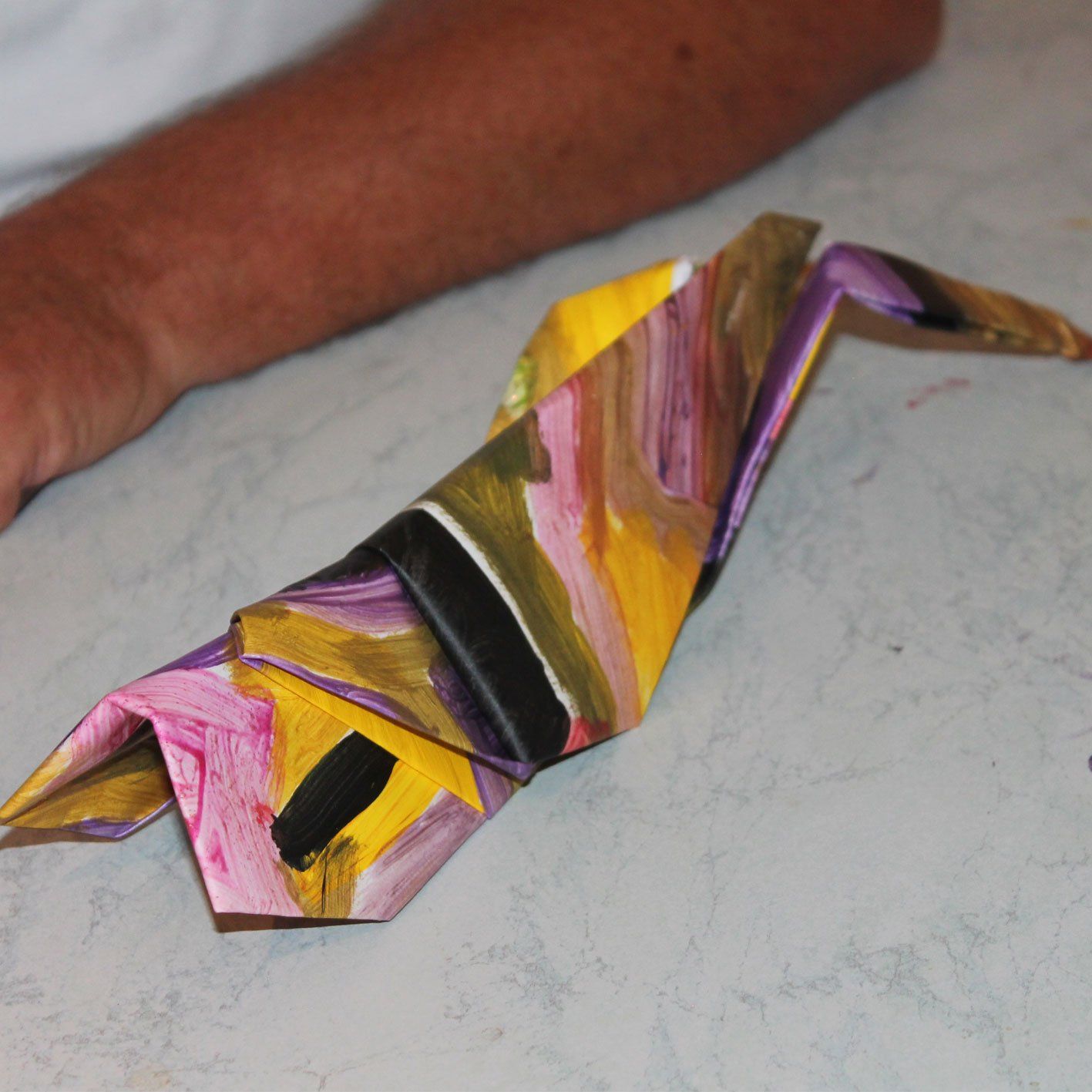 Een persoon houdt een kleurrijke origamivogel op een tafel