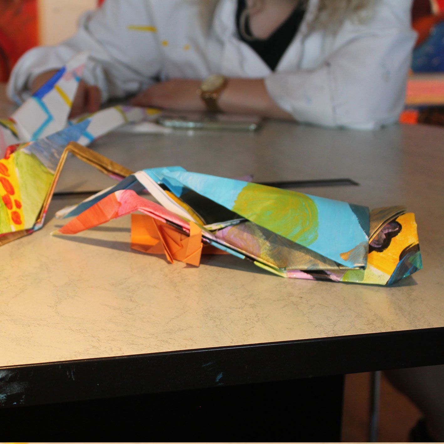 Een vrouw zit aan een tafel met origamivogels erop
