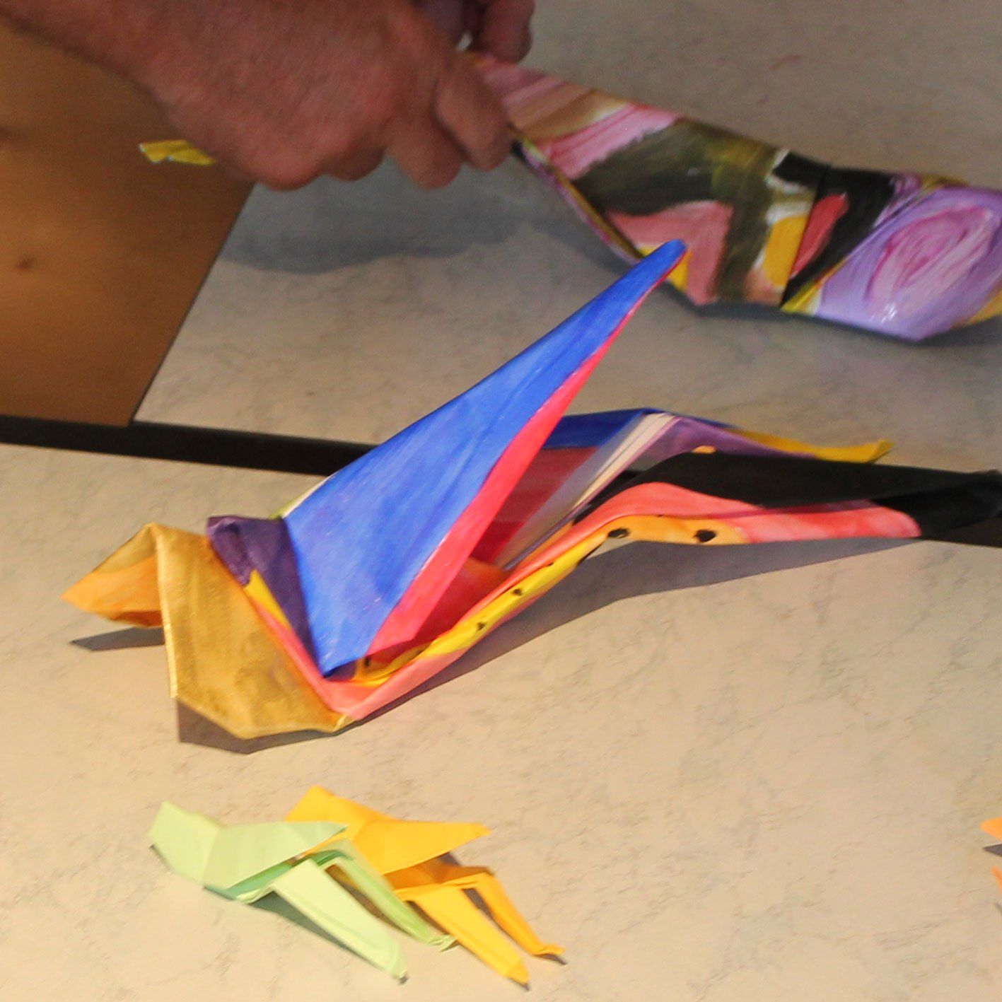 Een persoon maakt een kleurrijke origamisprinkhaan op een tafel
