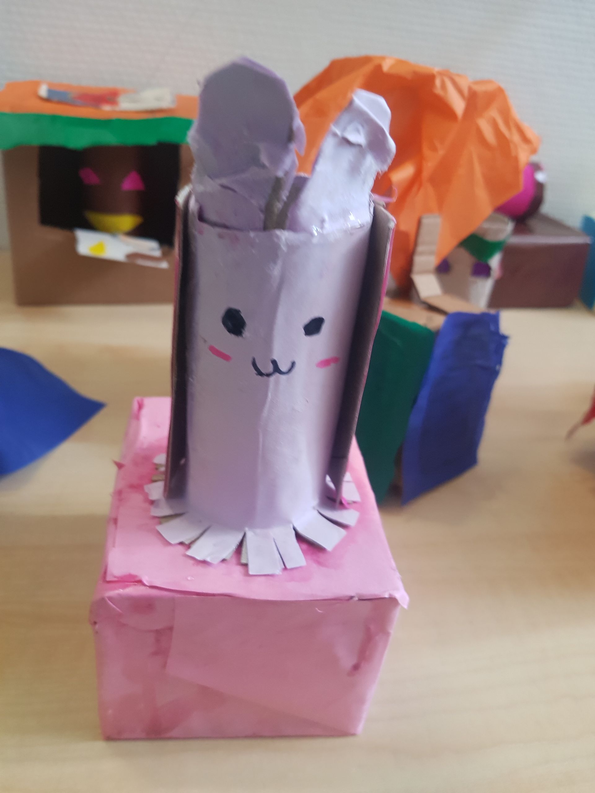 Een konijn gemaakt van toiletpapier zit op een roze doos