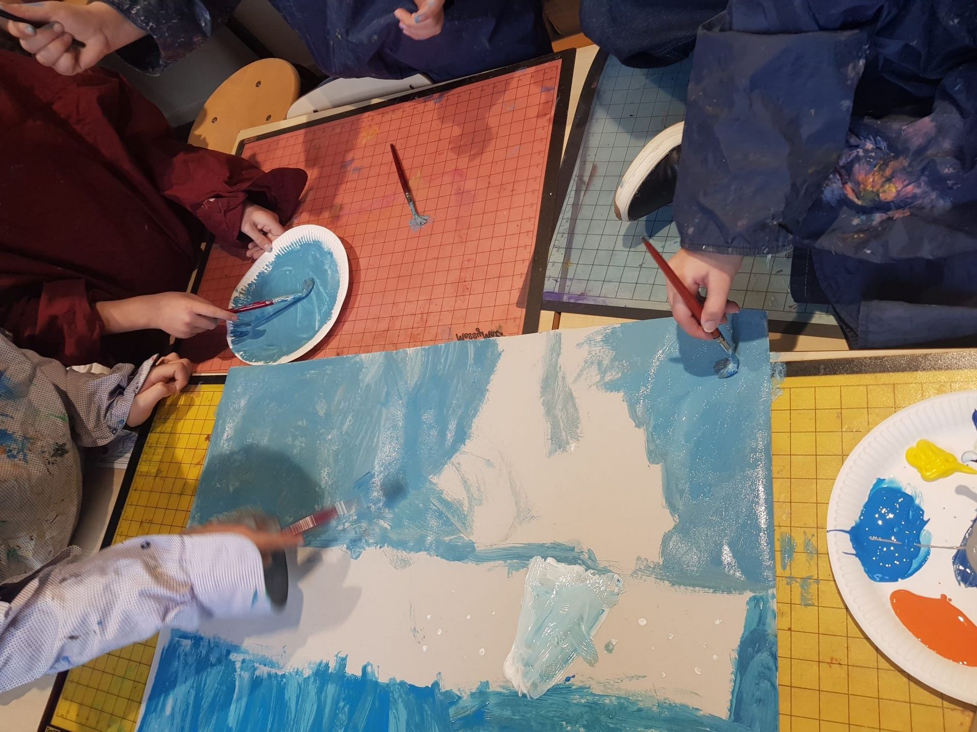 Een groep leerlingen schildert op een groot stuk papier