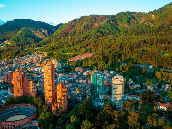 Vista aérea de Bogotá, Colombia, con edificios de la ciudad en primer plano y exuberantes montañas verdes en el fondo.