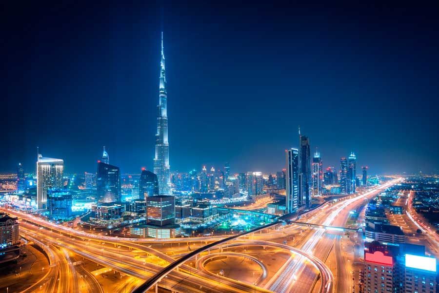 El horizonte de Dubai por la noche, dominado por el Burj Khalifa iluminado, con una compleja red de autopistas iluminadas debajo contra un cielo azul oscuro.