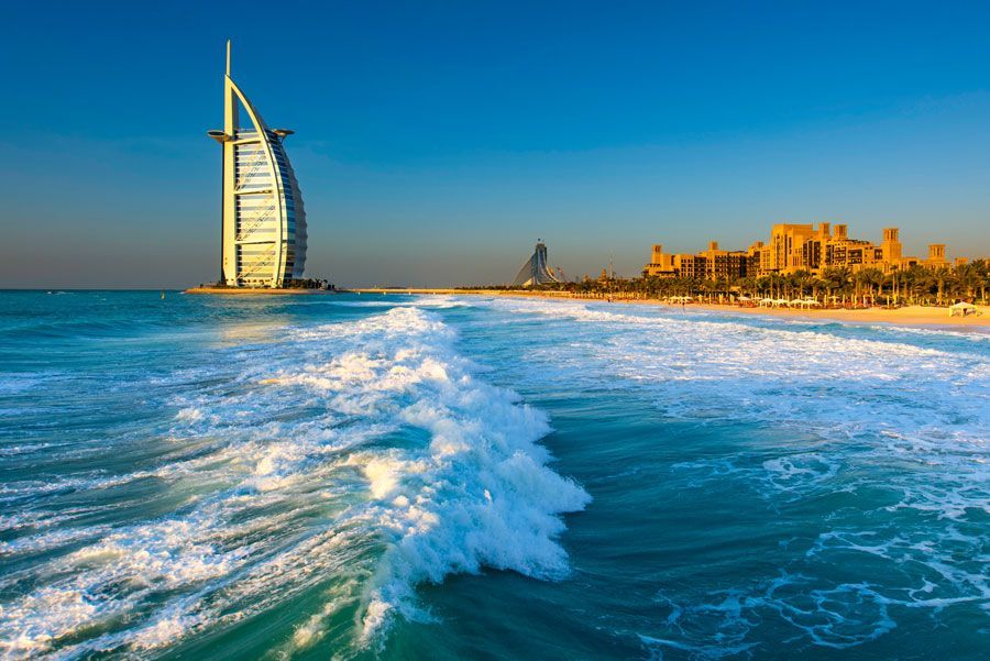 Hotel Burj Al Arab en Dubai en una playa soleada con agua turquesa y olas rompiendo en primer plano.