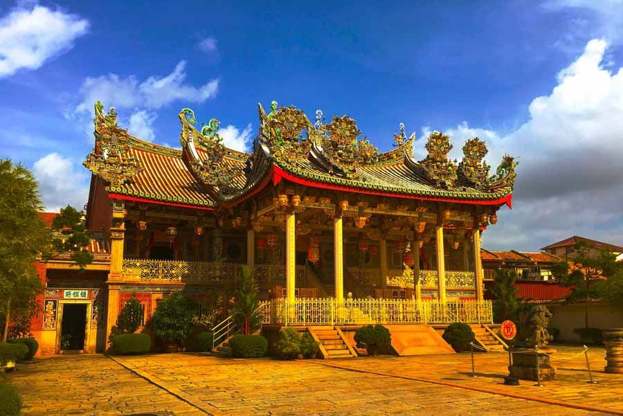 Templo chino adornado con techos tallados con gran detalle y columnas doradas contra un cielo azul.