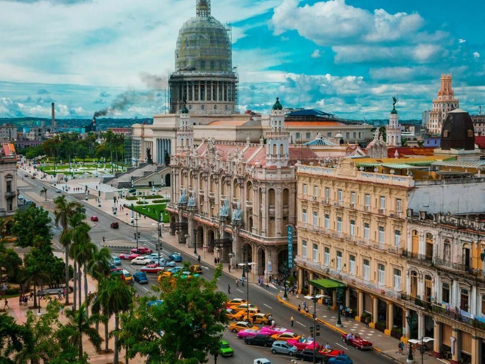 Paisaje urbano de La Habana, Cuba, con el edificio del Capitolio prominente, con autos coloridos y palmeras en un día soleado.