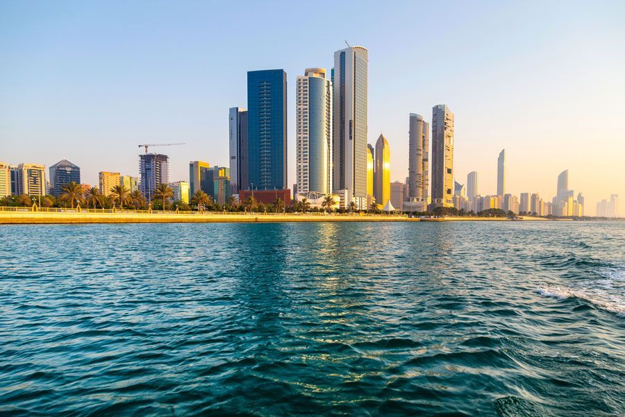 El horizonte de la ciudad, con altos edificios modernos a lo largo de una playa, se ve desde el agua turquesa. El cielo es azul claro.