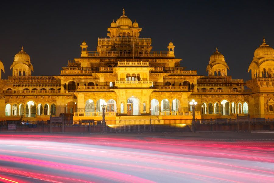 Edificio ornamentado iluminado por la noche con rayos de luz de los vehículos que pasan por delante; Jaipur, India.