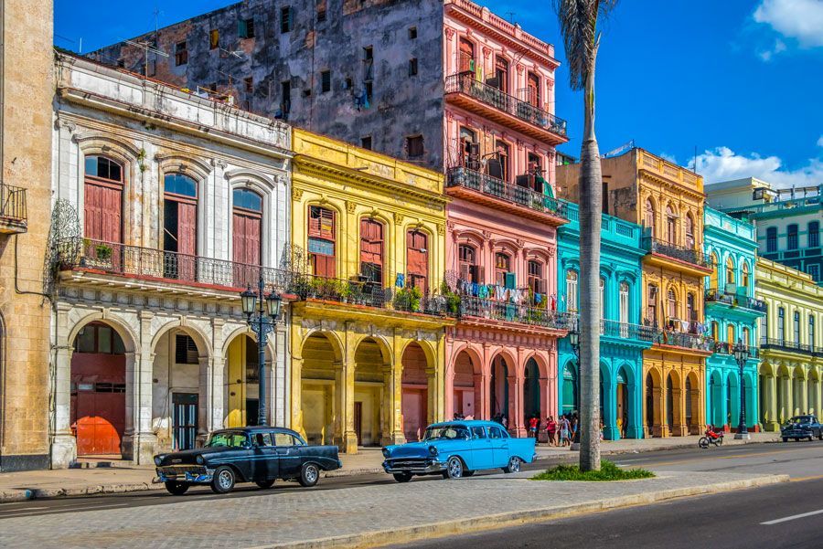 Fila de edificios de colores brillantes en La Habana, Cuba, con coches antiguos aparcados en el frente.