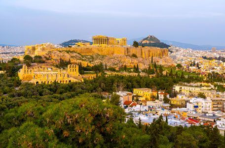 Una vista panorámica de la Acrópolis en Atenas, Grecia, que muestra ruinas antiguas en la cima de una colina, con una ciudad extendiéndose debajo.